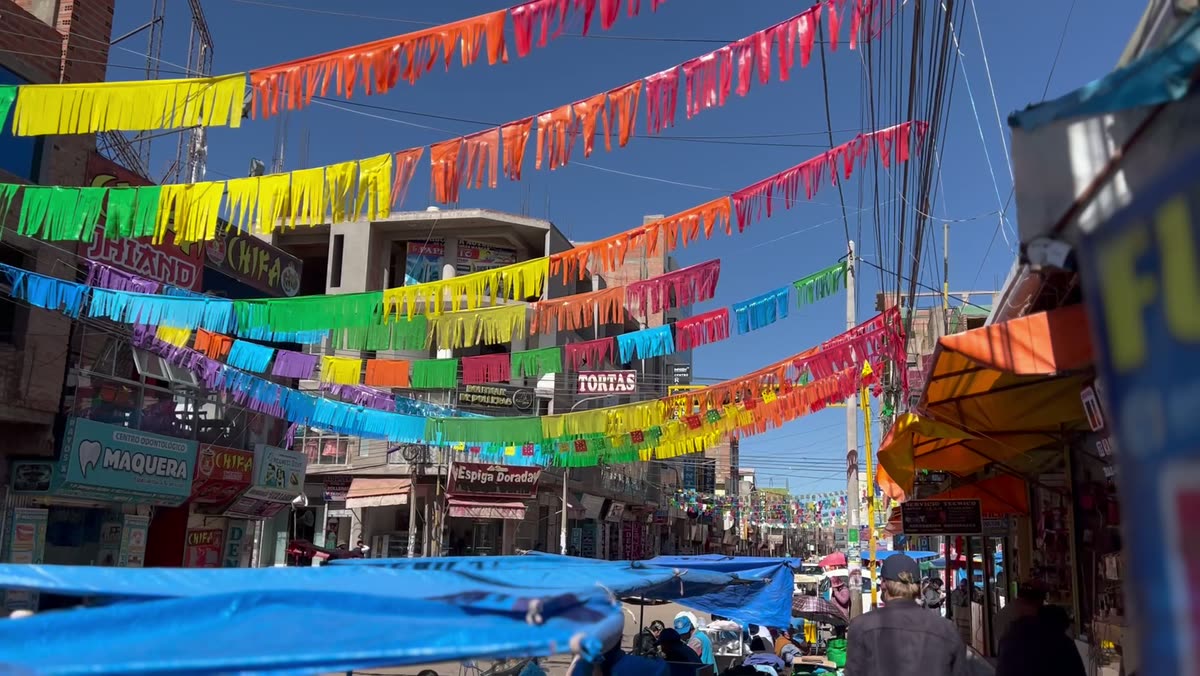 Un mercado callejero peruano bajo hileras de banderines de colores, con puestos bajo lonas azules